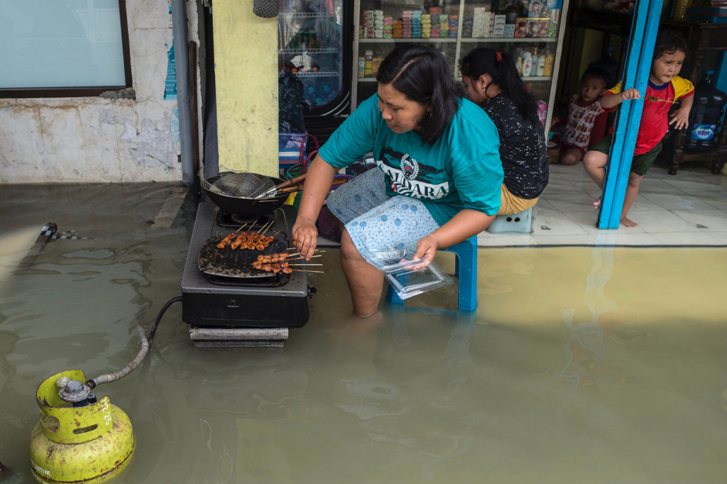 Warga memasak di luar tokonya yang terendam banjir di Gresik, Jawa Timur.
