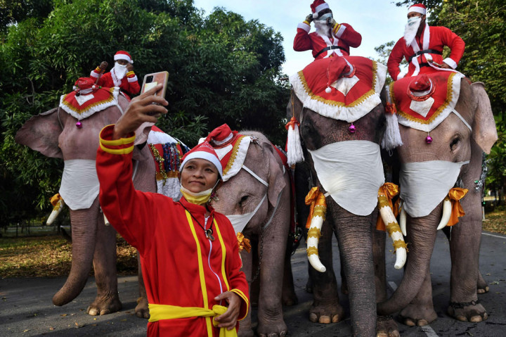 Natal dan kecintaan Thailand terhadap gajah berpadu pada Rabu, 23 Desember 2020 ketika empat makhluk raksasa yang berpakaian seperti Santa muncul di sebuah sekolah di luar Bangkok, lengkap dengan masker besar untuk mencegah virus korona (covid-19).