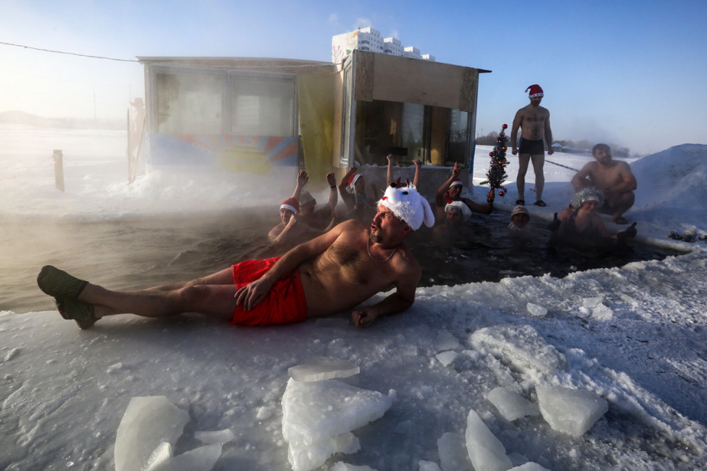 Seorang pria berbaring di atas es sementara anggota klub renang berenang di dalam air es saat suhu tubuh turun hingga 34 derajat celcius, di Novosibirsk, Rusia.