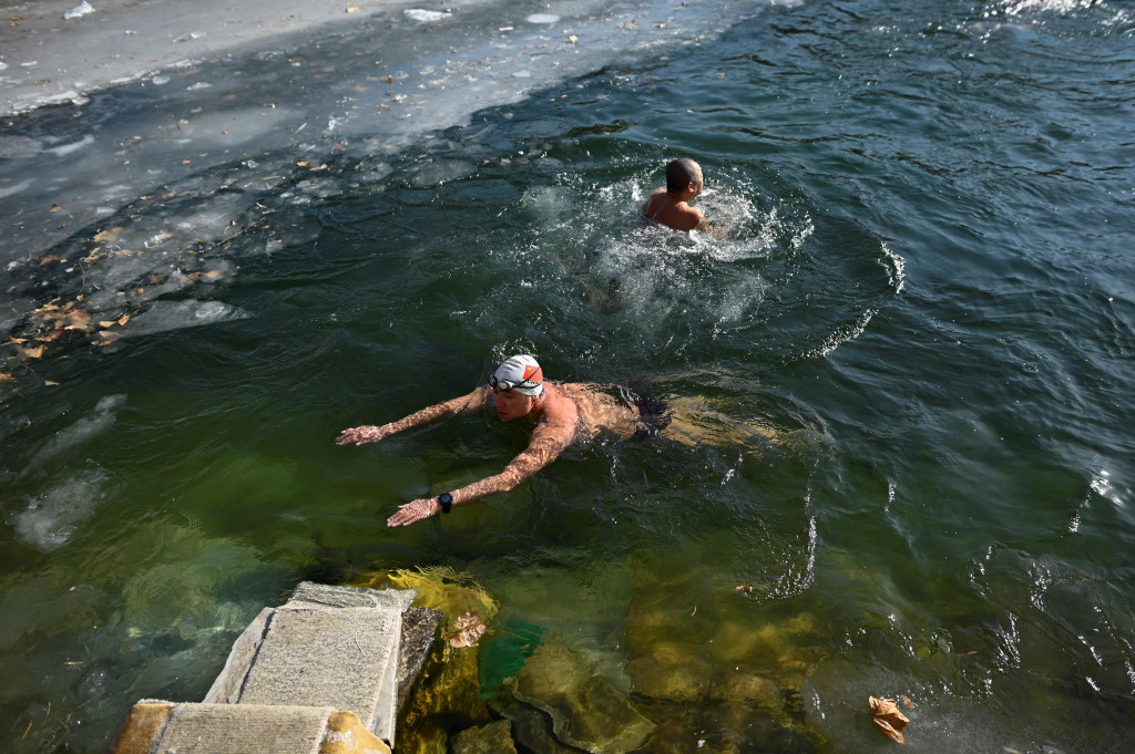 Dua perenang es berenang di perairan es dari danau beku pada hari musim dingin di Beijing, selasa, 6 Januari 2021.