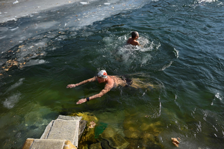 Dua perenang es berenang di perairan es dari danau beku pada hari musim dingin di Beijing, selasa, 6 Januari 2021.