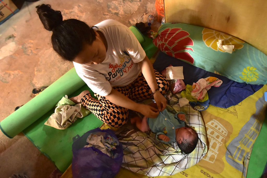 Armila tengah memakaikan baju untuk bayinya di posko pengungsian Kelurahan Binanga, Mamuju, Sulawesi Barat, Selasa, 19 Januari 2021.