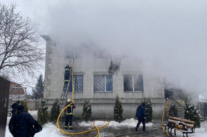 Asap mengepul dari jendela yang hangus di lantai dua gedung panti jompo di Ukraina, Kamis, 21 Januari 2021 waktu setempat, sementara petugas pemadam kebakaran dengan mantel tebal bekerja untuk madamkan api. Api berhasil dipadamkan dua jam setelah kejadian.