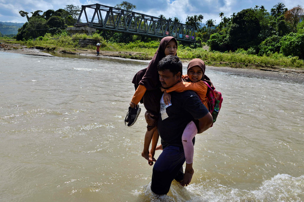 Warga menggendong anaknya saat menyeberangi sungai sepulang sekolah di wilayah pedalaman Desa Panca, Kecamatan Lembah Seulawah, Kabupaten Aceh Besar, Aceh, Jumat, 22 Januari 2021.