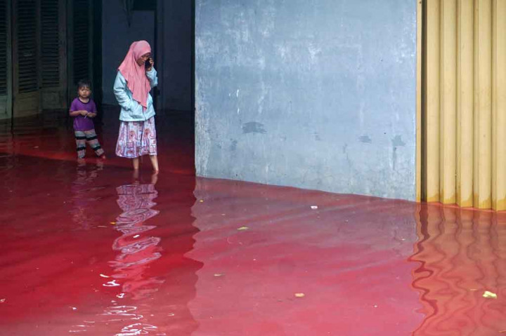 Warga melintasi ruas jalan yang digenangi banjir yang berwarna merah di Kelurahan Jenggot, Kecamatan Pekalongan Selatan, Kota Pekalongan, Jawa Tengah, Sabtu, 6 Februari 2021.