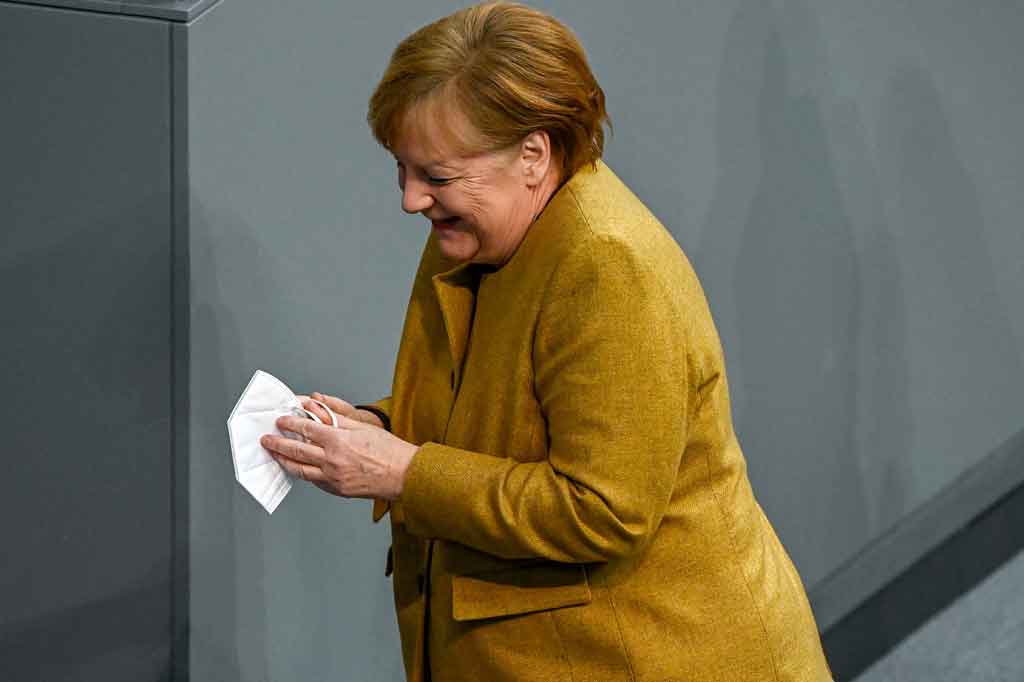 Menyadari hal tersebut, Merkel balik lagi ke arah meja sambil tersenyum untuk mengambil masker.