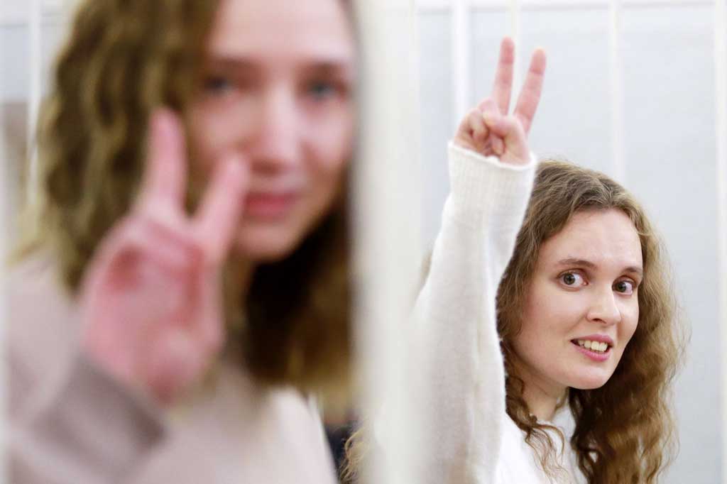 Jurnalis Belsat TV Katerina Bakhvalova (kanan) dan Daria Chultsova, yang ditahan sejak November usai melaporkan aksi protes anti-pemerintah , menunjukkan tanda V dari 'sangkar' terdakwa selama proses persidangan di Minsk, Belarusia pada Kamis, 18 Februari 2021.