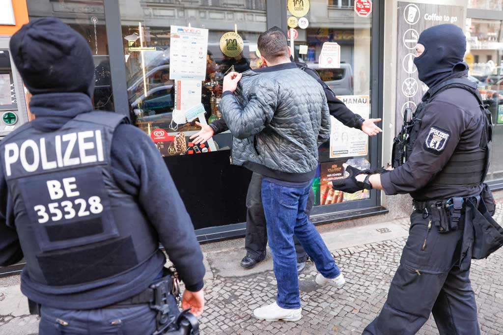 Polisi bersenjata dan mengenakan penutup kepala mengawal seorang pria di depan sebuah gedung di distrik Neukoelln, Berlin selama penggerebekan terhadap kriminalitas klan terorganisir pada Kamis, 18 Februari 2021.