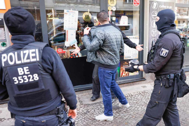 Polisi bersenjata dan mengenakan penutup kepala mengawal seorang pria di depan sebuah gedung di distrik Neukoelln, Berlin selama penggerebekan terhadap kriminalitas klan terorganisir pada Kamis, 18 Februari 2021.