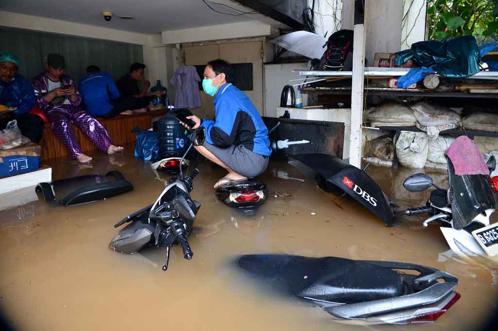 Warga duduk-duduk menghindari air banjir di Kemang, Jakarta Selatan, sementara beberapa sepeda motor terendam.
