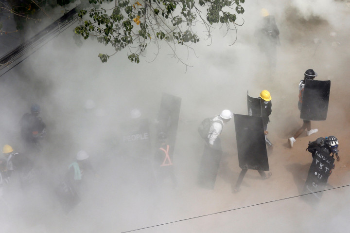 Para pengunjuk rasa beraksi ketika mereka diliputi oleh gas air mata yang ditembakkan oleh polisi dan ketika pengunjuk rasa lainnya melepaskan alat pemadam kebakaran, selama demonstrasi menentang kudeta militer di Yangon.
