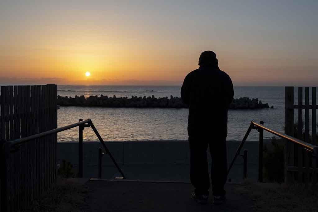 Saat matahari terbit di Hisanohama prefektur Fukushima, Toshio Kumaki yang berusia 78 tahun berjalan di sepanjang tembok laut raksasa yang dibangun setelah tsunami dan berdoa. Mata Kumaki berkaca-kaca saat mengingat bencana itu.