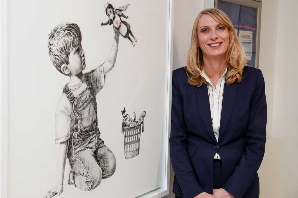 
Lukisan cat minyak yang ditandatangani oleh seniman yang identitasnya disembunyikan tersebut menunjukkan seorang anak laki-laki tengah bermain dengan memegang boneka perawat superhero, sementara tokoh Batman dan Superman berada ke tempat sampah di sampingnya. 