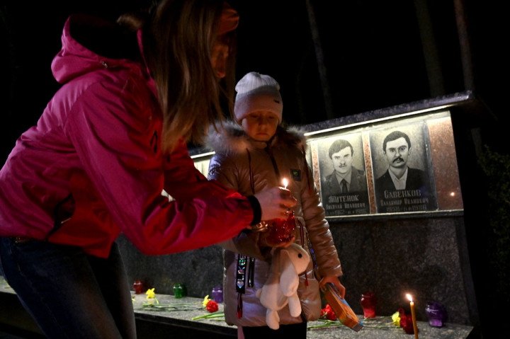 Seorang wanita dan putrinya menyalakan lilin di monumen korban Chernobyl di Slavutych, Ukraina, Minggu, 25 April 2021.