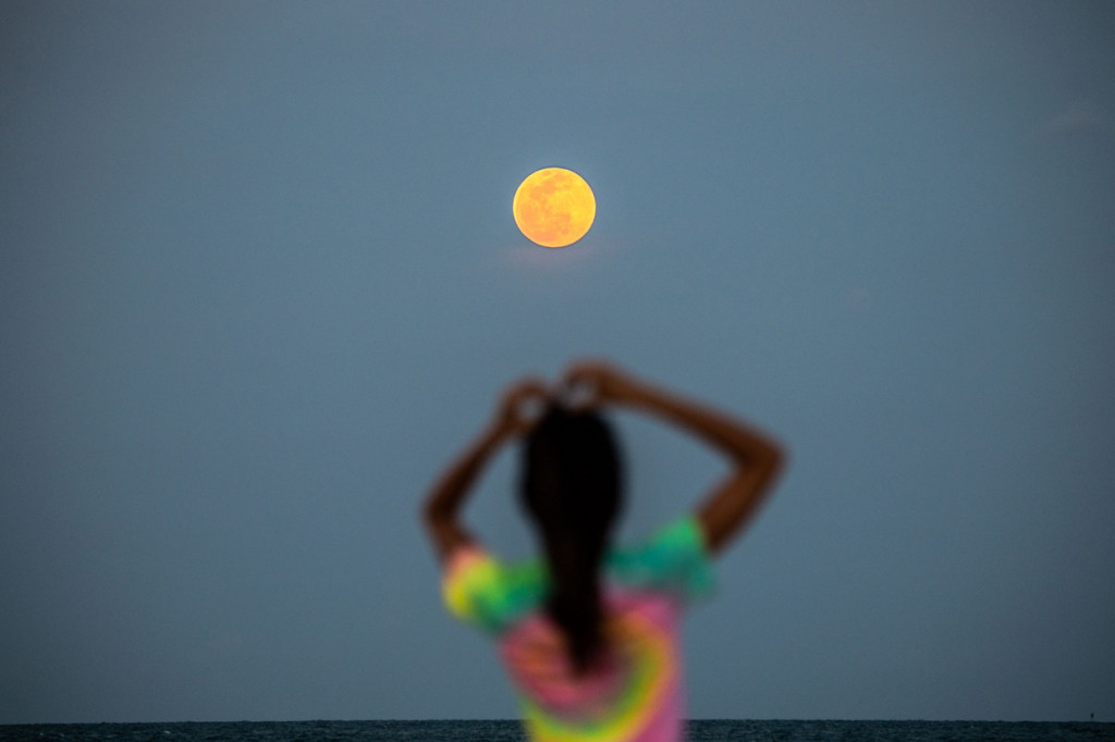 Bulan Purnama Super Pink terlihat di latar belakang saat orang-orang bersantai di pantai di Miami Beach, Florida. AFP Photo/Chandan Khanna