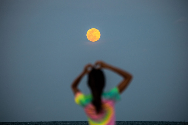 Bulan Purnama Super Pink terlihat di latar belakang saat orang-orang bersantai di pantai di Miami Beach, Florida. AFP Photo/Chandan Khanna