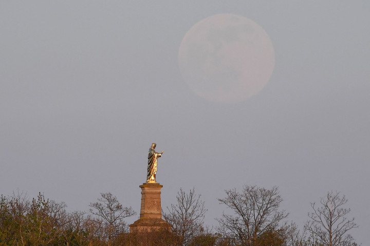 Bulan Purnama Super Pink muncl di belakang patung Kristus di Wolxheim, Prancis Timur. AFP Photo/Patrick Hertzog