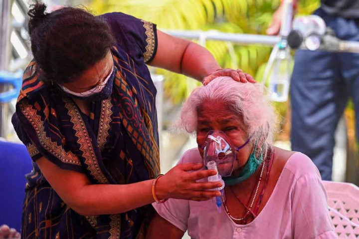 Seorang warga menghela nafas lega saat masker dipasang di wajah ibunya, sehingga memungkinkan penderita covid-19 dapat menghirup oksigen sambil duduk di pinggir jalan yang sibuk di pinggiran New Delhi.