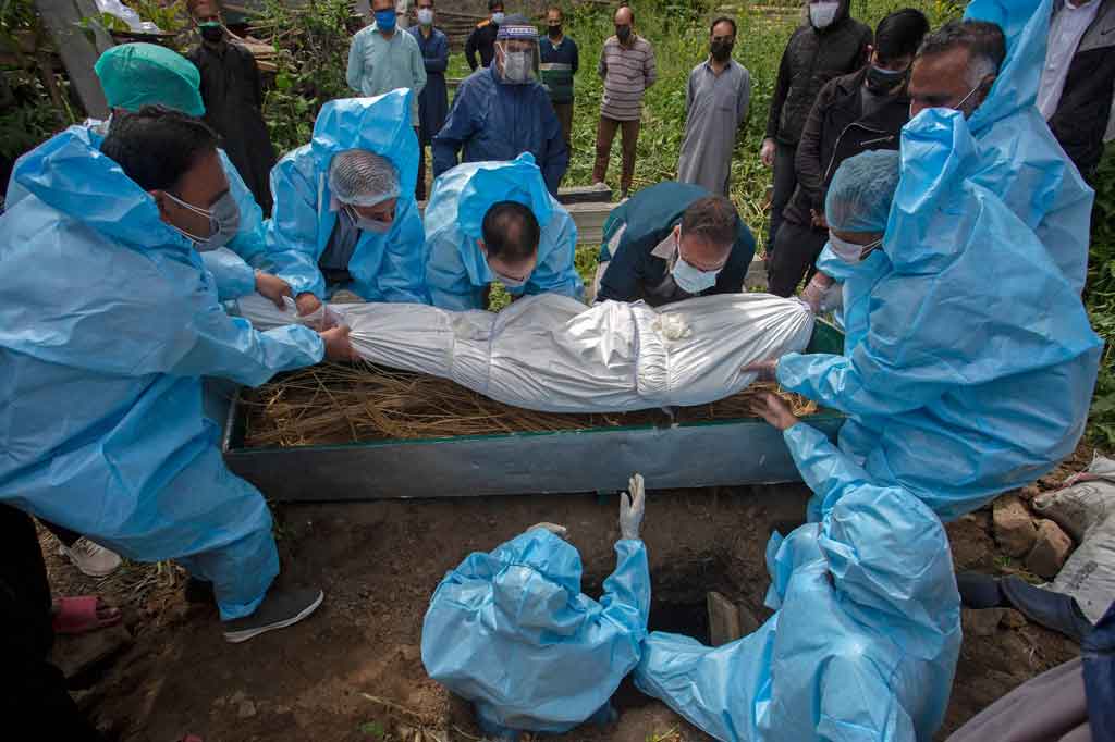 Kerabat yang mengenakan alat pelindung memakamkan jenazah yang positif Covid-19 saat prosesi pemakaman di Srinagar, India pada Jumat, 7 Mei 2021.