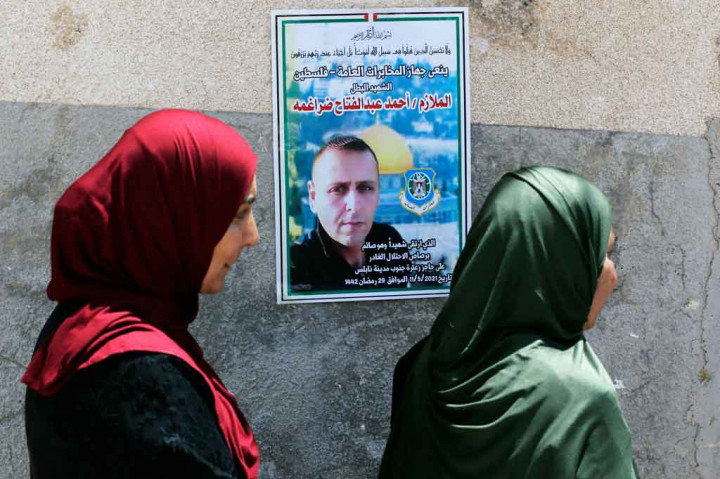 Kerabat Ahmed Daraghmeh, berdiri di dekat poster yang menggambarkan dia yang dipajang di dinding saat mereka berduka selama pemakamannya di kota al-Lubban al-Sharqiya dekat Nablus pada 12 Mei 2021.