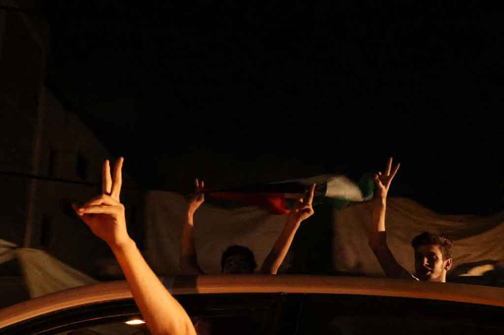 Warga yang berada di depan bangunan yang hancur menunjukkan tanda V untuk kemenangan saat mereka merayakan gencatan senjata antara Israel dan dua kelompok bersenjata utama Palestina, di Gaza pada Kamis, 20 Mei 2021 waktu setempat.