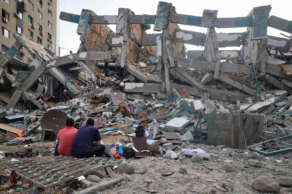 Sementara ada warga yang duduk-duduk sambil melihat bangunan rumahnya yang hancur akibat serangan Israel.