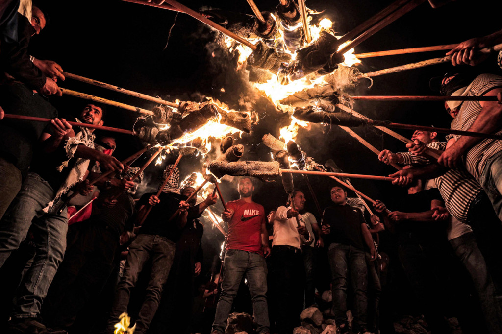 Pengunjuk rasa Palestina berkumpul membawa obor selama demonstrasi menentang pos pemukim Israel di Eviatar, di kota Beita, dekat kota Nablus, Tepi Barat yang diduduki, pada 3 Juli 2021. Seorang pria Palestina tewas tertembak oleh tentara Israel di Tepi Barat. Insiden terjadi saat bentrok antara warga Palestina dan pemukim Yahudi memanas.
