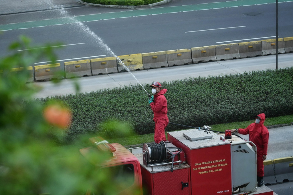 Petugas pemadam kebakaran melakukan penyemprotan di Jalan Jenderal Sudirman, Jakarta, Minggu, 4 Juli 2021.