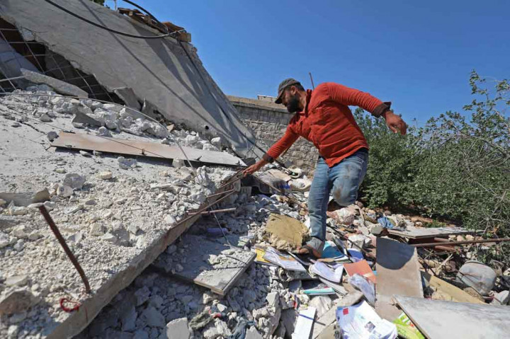 Seorang pria berjalan di atas reruntuhan sebuah rumah yang hancur akibat penembakan artileri rezim Suriah di Desa Iblin, wilayah Jabal al-Zawiya, Provinsi Idlib barat laut yang dikuasai pemberontak, pada Kamis, 22 Juli 2021.