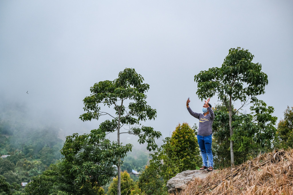Warga menggunakan gawai di sebuah bukit yang mampu menangkap sinyal internet di Desa Matantimali, Marawola Barat, Kabupaten Sigi, Sulawesi Tengah.