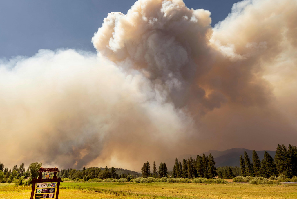 Tanda selamat datang di Greenville terlihat di depan kepulan asap yang mengepul saat api Dixie membakar dekat kota Greenville, California, Rabu, 3 Agustus 2021.