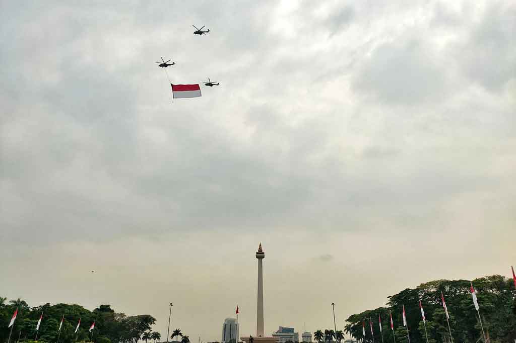 Tampak tiga helikopter TNI AU terbang, salah satunya dengan bendera Merah Putih raksasa mengelilingi langit Ibu Kota.
