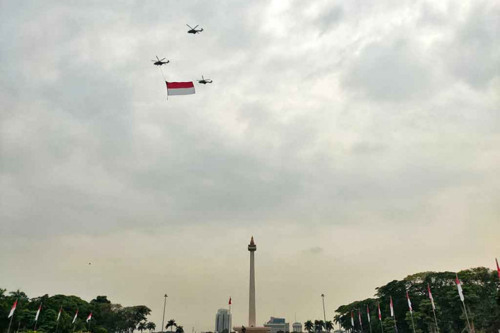 Tampak tiga helikopter TNI AU terbang, salah satunya dengan bendera Merah Putih raksasa mengelilingi langit Ibu Kota.