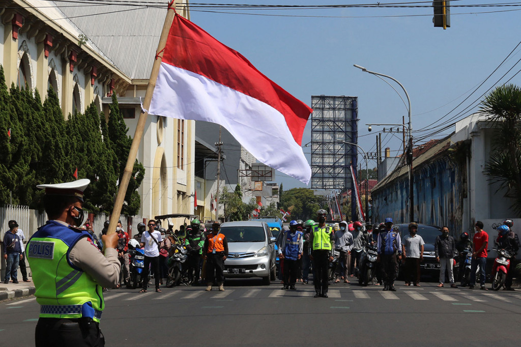 Pengendara berhenti untuk memberi hormat kepada bendera merah putih di sepanjang jalan di Malang pada 17 Agustus 2021, untuk memperingati HUT ke-76 RI. AFP Photo/Aman Rochman