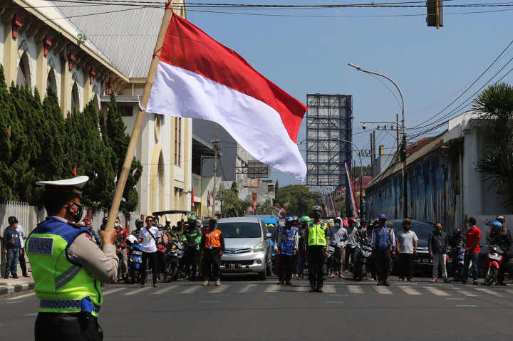 Pengendara berhenti untuk memberi hormat kepada bendera merah putih di sepanjang jalan di Malang pada 17 Agustus 2021, untuk memperingati HUT ke-76 RI. AFP Photo/Aman Rochman