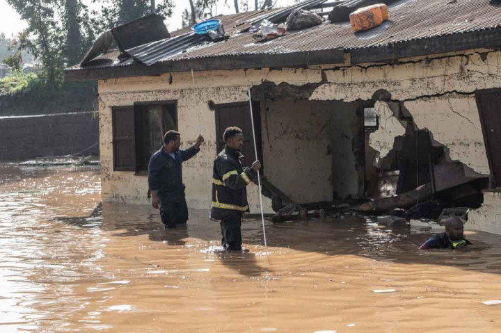 Gambar dari ibu kota menunjukkan petugas pemadam kebakaran mengarungi air cokelat untuk memeriksa rumah-rumah yang terendam banjir dan berjalan melalui lumpur dengan tandu untuk mengevakuasi jenazah.