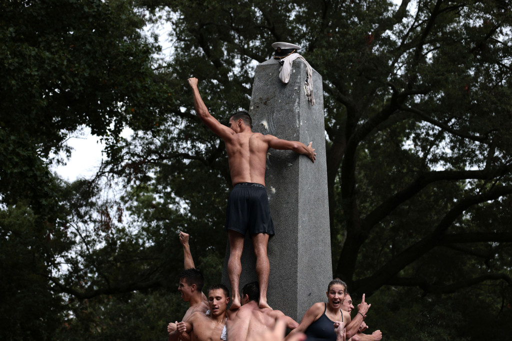 Taruna kelas 2 James Crossfield mengangkat tangan usai menempatkan topi kakak kelasnya pada puncak Monumen Herndon di Akademi Angkatan Laut AS, di Annapolis, Maryland.