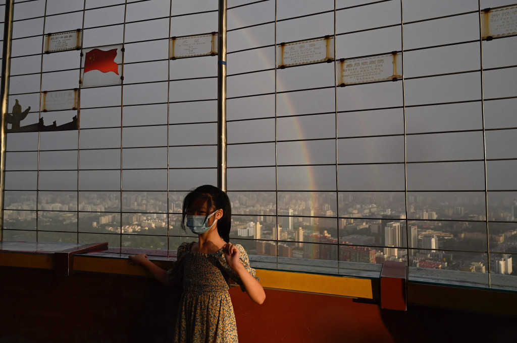 Seorang warga saat berfoto berlatar belakang pelangi ganda yang terlihat dari Central Television Tower di Beijing, Tiongkok.