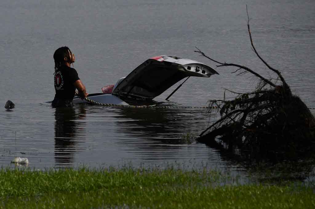 Seorang pria menggunakan tali untuk mencoba menarik mobil yang terendam banjir pasca-Badai Ida menerjang LaPlace, Louisiana, Amerika Serikat pada 30 Agustus 2021 waktu setempat.
