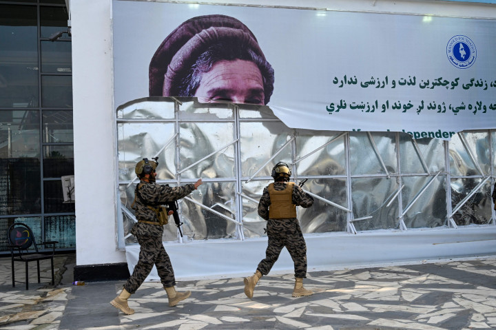 Anggota unit militer Taliban Badri 313 berjalan melewati spanduk robek yang menampilkan gambar mendiang pemimpin Mujahidin Afghanistan Ahmed Shah Massoud saat mereka tiba di bandara di Kabul pada 31 Agustus 2021, setelah tentara Amerika Serikat (AS) terakhir meninggalkan Afghanistan.