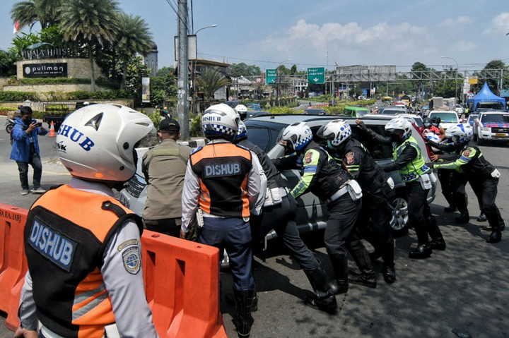 Petugas gabungan saat membantu mendorong kendaraan roda 4 dengan plat nomer genap yang mogok saat diminta putar balik di Simpang Gadog, Bogor, Jawa Barat, Jumat, 3 September 2021.