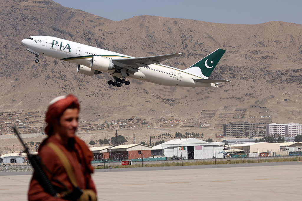 Seorang milisi Taliban berjaga-jaga saat pesawat Pakistan International Airlines (PIA), penerbangan internasional komersial pertama yang mendarat sejak Taliban merebut kembali kekuasaan bulan lalu, lepas landas dengan penumpang di bandara di Kabul pada Senin, 13 September 2021.