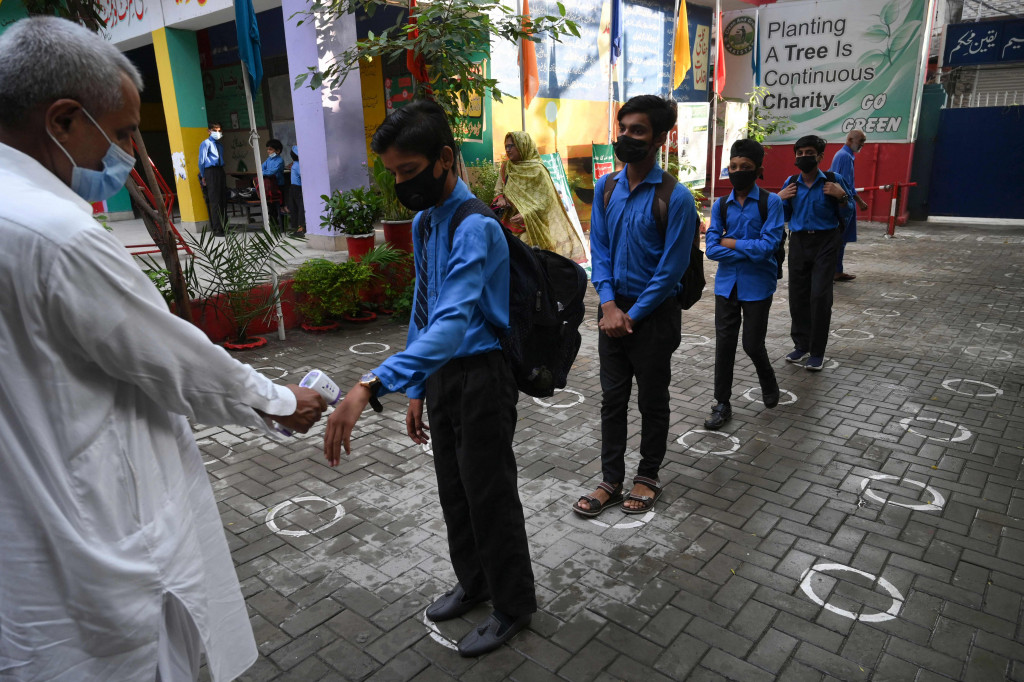 Seorang guru memeriksa suhu tubuh siswa ketika mereka tiba di sekolah di Lahore, Kamis, 16 September 2021.