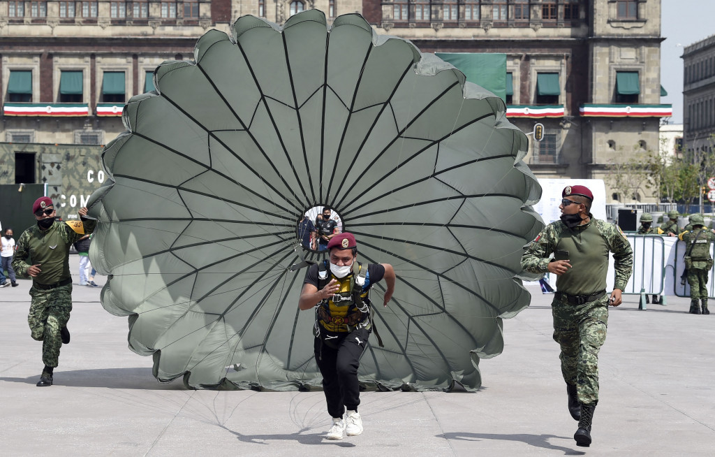 Pasukan terjun payung membantu seorang pria berlari dengan parasut terbuka dalam pameran yang disebut The Great Force of Mexico di Alun-alun Zocalo, Mexico City, Meksiko, 20 September 2021.