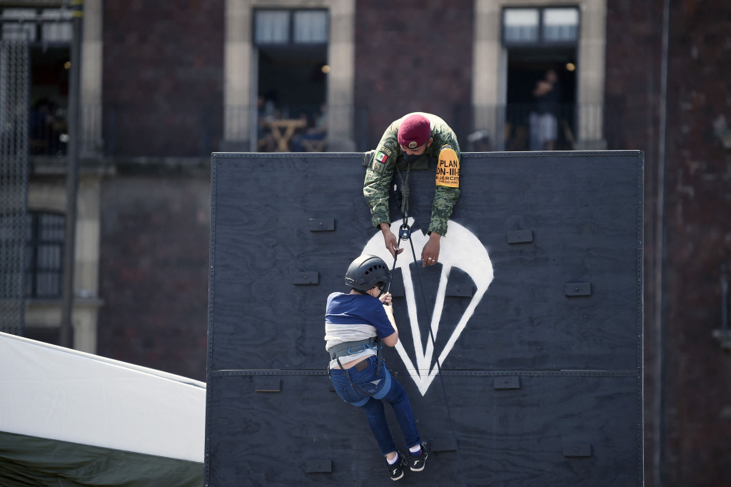 Seorang penerjun payung membantu seorang gadis memanjat dinding dalam pameran yang disebut The Great Force of Mexico di Alun-alun Zocalo, Mexico City, Meksiko, 20 September 2021.