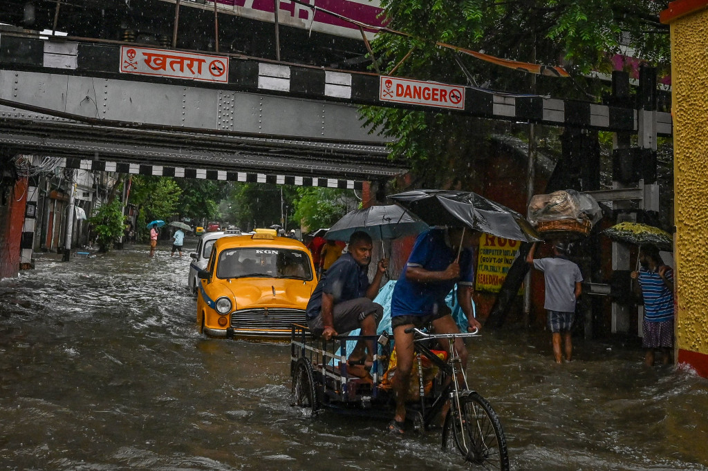 Pengendara melewati jalan yang tergenang air di tengah hujan lebat di Kolkata.