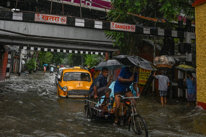 Pengendara melewati jalan yang tergenang air di tengah hujan lebat di Kolkata.