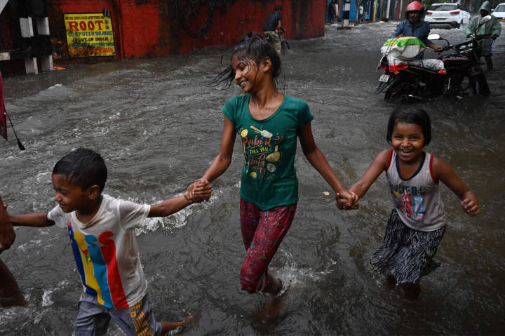 Anak-anak melewati jalan yang tergenang air setelah hujan deras di Kolkata.