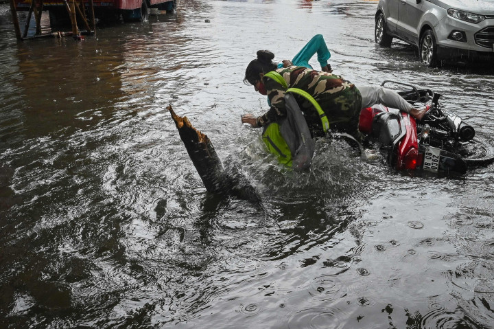 Seorang pengendara sepeda motor terjatuh saat melintasi jalan yang tergenang air setelah hujan deras di Kolkata.
