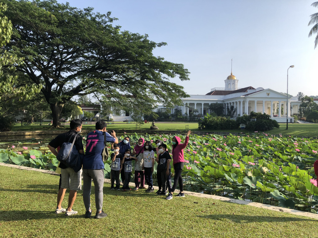 Warga berfoto dengan latar Istana Bogor saat berwisata ke Kebun Raya Bogor, Jawa Barat, Minggu, 26 September 2021. 